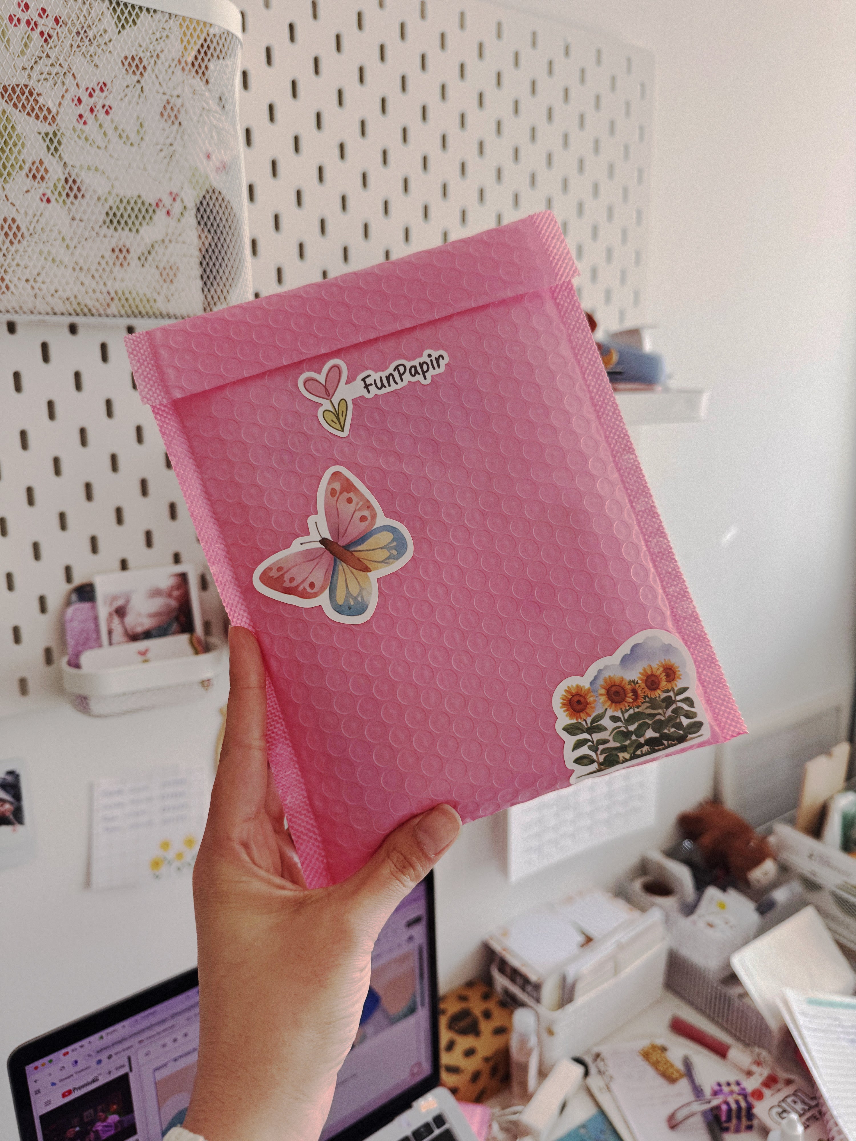 Pink bubble mailer with stickers featuring a butterfly and flowers, held by a hand.