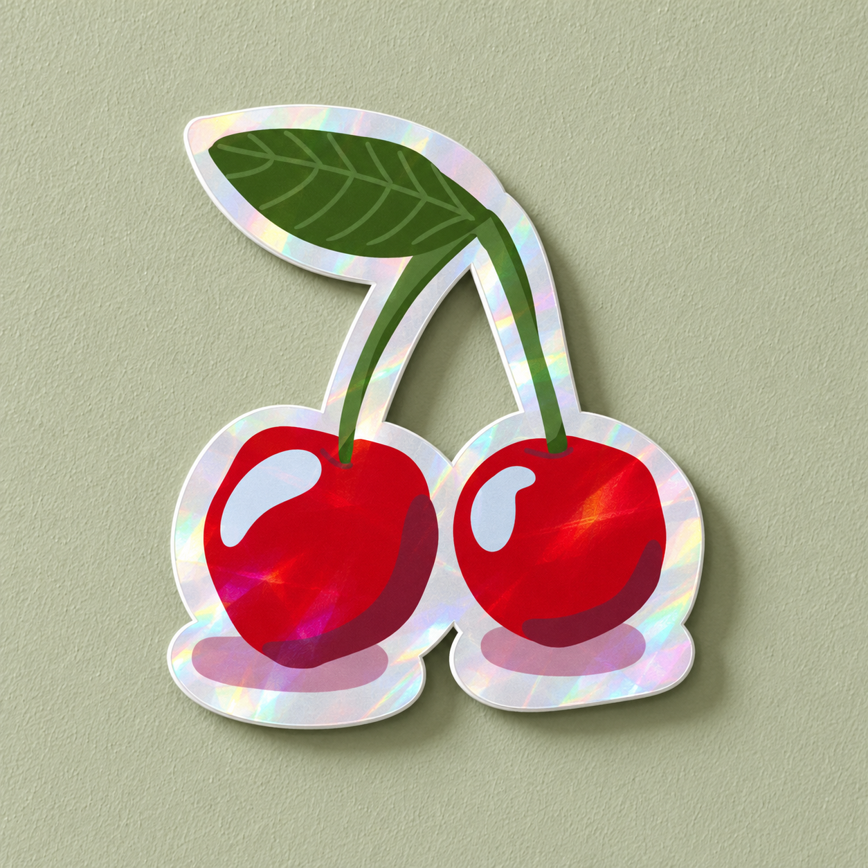 A die-cut holographic sticker of two red cherries with green stems and leaves, shown on a textured sage green background.
