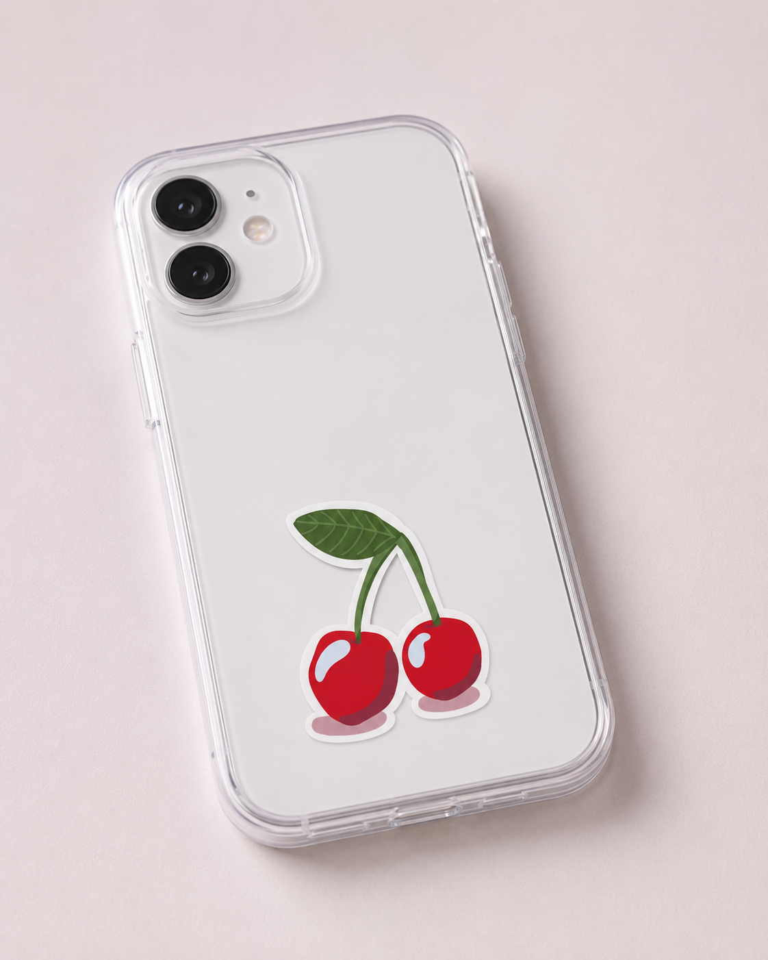 A clear protective phone case on a white smartphone, featuring a graphic of two red cherries with green stems and leaves on the back, set against a light pink background.