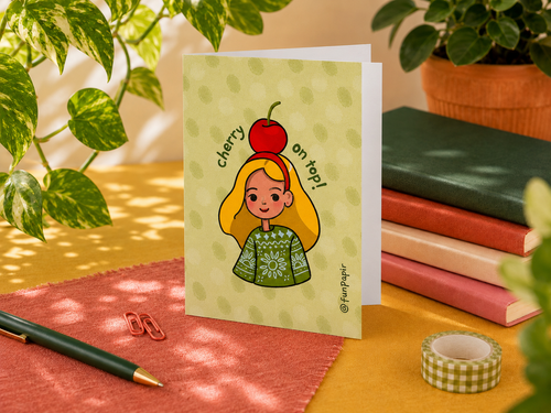 A greeting card with a cute illustration of a girl with a red cherry on her head, standing on a desk surrounded by plants, notebooks, and stationery.