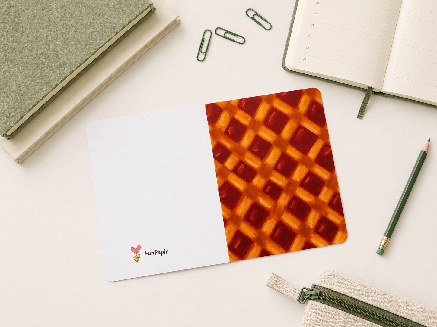 A flat-lay view of a notepad with a split design: one half is white with the 'FunPeople' logo, and the other half features a red and orange waffle pattern. The notepad is styled on a white desk with a pencil, paperclips, notebooks, and a zipper pouch.