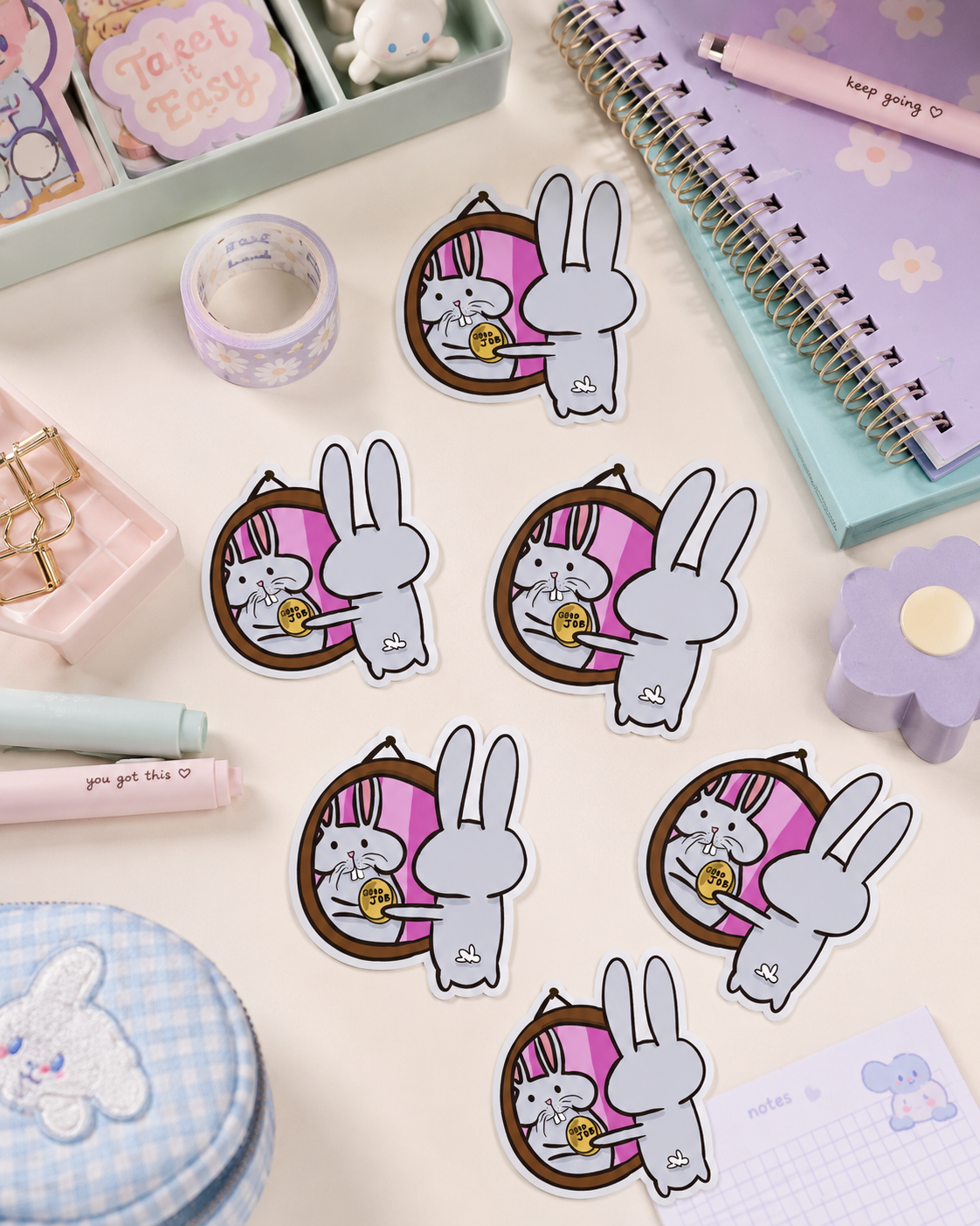 A set of cute cartoon bunny stickers arranged on a pastel desk flat-lay. The stickers feature a white bunny in a pink basket holding a yellow moon, surrounded by matching pastel stationery items like a notebook, washi tape, and a pencil case.
